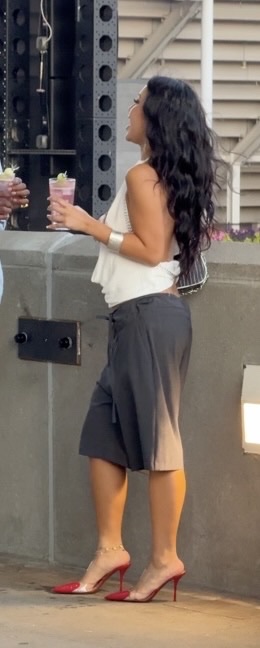 White halter top, charcoal capri pants, red mule heels with ankle bracelet, holding a pink drink.